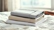 © AsgilCreative - Neatly Stacked Gray Beige and White Sheets on Textured Bedding in Bright Room with Soft Natural Light Near Window Minimalist Style