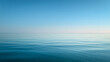 © Broccolini - A serene wide-angle view of a calm turquoise ocean with a clear horizon line under a soft blue sky and gentle white clouds, creating a peaceful and minimalist landscape.