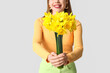 © Pixel-Shot - Young woman with bouquet of beautiful daffodil flowers on grey background