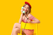 © Pixel-Shot - Young woman talking by retro telephone on chair against yellow background. International Women's Day