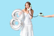 © Pixel-Shot - Young woman talking by retro telephone with air balloon in shape of figure 8 on blue background. International Women's Day