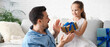 © Pixel-Shot - Little daughter giving father present in living room. Father's Day celebration