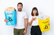 © luismolinero - Young couple holding a bag full of plastic and paper to recycle isolated on white background with surprise and shocked facial expression