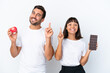 © luismolinero - Young couple holding chocolate and apple isolated on white background showing and lifting a finger in sign of the best