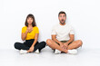 © luismolinero - Young couple sitting on the floor isolated on white background with surprise and shocked facial expression