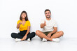 © luismolinero - Young couple sitting on the floor isolated on white background shaking hands for closing a good deal