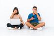 © luismolinero - Young couple sitting on the floor holding pc and mobile phone isolated on white background covering mouth with hands for saying something inappropriate