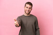 © luismolinero - Young caucasian man isolated on pink background shaking hands for closing a good deal
