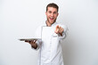 © luismolinero - Young caucasian chef with tray isolated on white background surprised and pointing front