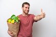 © luismolinero - Young caucasian man holding a grocery shopping bag isolated on white background giving a thumbs up gesture