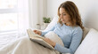 © OlgaNeuroArt - Young woman reading a book in bed. Relaxed female sitting in a bright bedroom with a book. Morning leisure and rest at home. Lifestyle concept of quiet time and education