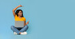 © Prostock-studio - Happy young black woman sitting on floor with brand new laptop, pointing and looking at copy space over blue studio background, pretty african american lady using notebook, panorama