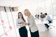 © deagreez - Two professional women discussing business ideas with digital tablet in an open office workspace during a collaborative meeting
