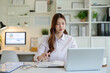 © wattana - Focused businesswoman working on a laptop while writing in a notebook at a modern office desk