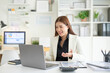 © wattana - Smiling businesswoman discussing financial data during an online meeting, working with a laptop and accounting documents in a modern office.