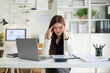 © wattana - Stressed accountant holding her head while reviewing financial documents at the desk,  work pressure during tax season and financial deadlines.