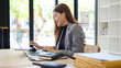 © wattana - Smiling businesswoman working on a laptop at a desk in a modern office.