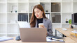 © wattana - Businesswoman drinking coffee while working on a laptop in a modern office.