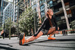 © deagreez - Young woman stretches outdoors in urban park wearing sportswear during a sunny morning fitness routine in the city