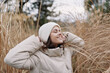 © SHOTPRIME STUDIO - Woman in a warm beige coat and knit hat enjoying outdoor winter scenery among tall grass, relaxed smile, soft natural light, candid portrait capturing comfort and seasonal calm.