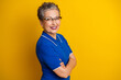 © deagreez - Mature woman with short gray hair and glasses smiles confidently in a blue polo against a bright yellow background