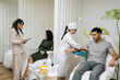 © dikushin - Wide shot of medical professional in uniform and gloves prepares male patient arm for blood draw while colleague having consultation with client in background, depicting routine diagnostic testing.