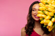 © Home-stock - Women's Day celebration. Happy lady posing with bouquet of yellow tulips near face, looking aside at free space and smiling, standing isolated on pink background