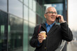 © Jelena - Senior businessman talking on smartphone holding coffee cup