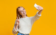© Prostock-studio - Smiling teenage girl taking selfie on smartphone, showing peace gesture, orange studio background with copy space