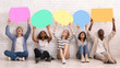 © Prostock-studio - Multiracial group of teenagers sitting on floor and holding colorful speech bubbles above, panorama