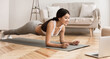 © Prostock-studio - Online Training. Woman Exercising at Home, Doing Plank and Watching Videos on Laptop