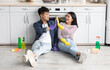 © Prostock-studio - Good job. Tired asian couple in rubber gloves sitting on floor next to stove among house-keeping supplies in cozy kitchen, giving high five and smiling, resting after cleaning apartment, copy space