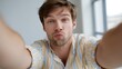 © JuliaDorian - Handsome man taking a selfie with a playful expression while wearing a striped shirt in a bright indoor setting with natural light