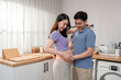 © Kawee - Asian husband and pregnant wife standing together in kitchen at home.