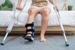 © Kawee - Close up of injured woman wearing splint on leg in cozy bedroom at home.
