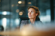 © EricMiguel - Confident middle - aged businesswoman in grey textured blazer seated at boardroom head, thoughtful upward gaze and soft bokeh office lights