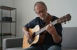 © Generative AI - Focused mature man playing an acoustic guitar while sitting comfortably on a couch, enjoying a musical hobby at home.