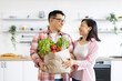 © sofiko14 - An Asian couple smiles while holding a bag of fresh produce in their bright, modern kitchen