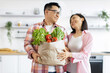 © sofiko14 - A smiling couple carries a bag of fresh produce together in their kitchen