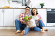 © sofiko14 - An Asian couple smiles while holding a bag of fresh produce in their modern kitchen