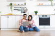 © sofiko14 - An Asian couple smiles while looking at a laptop computer in their modern kitchen