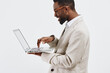 © SHOTPRIME STUDIO - Professional young man using a laptop computer, wearing glasses and a beige blazer, standing against a plain white background. Male office worker or freelancer, technology, work, modern lifestyle