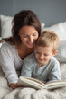 © rabbit75_fot - Mothers Day, Valentines Day, love holiday theme. A woman and a young boy lying on a bed, engrossed in a book. The woman, wearing a white shirt, has a warm smile on her face.