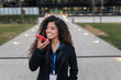 © CatalnIlie - Young professional woman talking on phone with speaker in urban business district, smiling and communicating