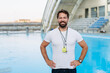 © Halfpoint - Professional swimming coach standing by outdoor pool.