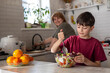 © Светлана Мищенко - young boy mixes a fresh vegetable salad in a bright home kitchen while an older family member prepares food in the background. Everyday family cooking moment focused on healthy eating, learning basic