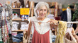 © JackF - Glad old-aged female customer reviewing summer dresses during shopping in clothing store