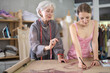 © JackF - Elderly woman teaches young woman how to draw pattern on paper in sewing workshop