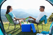 © New Africa - Couple and cool box with bottles of beer in mountains, view from tent