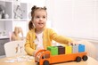 © New Africa - Cute little girl playing with toys at wooden table indoors
